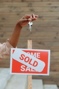 A hand holding keys above a sold sign in a real estate environment, symbolizing a completed property sale.
